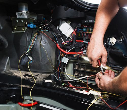 A man is working on the inside of a car with a pair of pliers.
