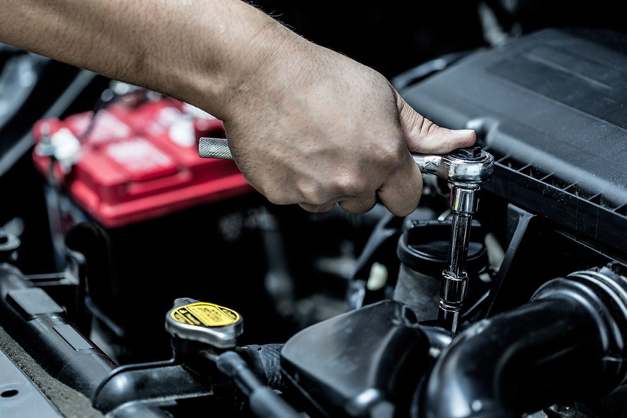 A person is working on a car engine with a wrench.