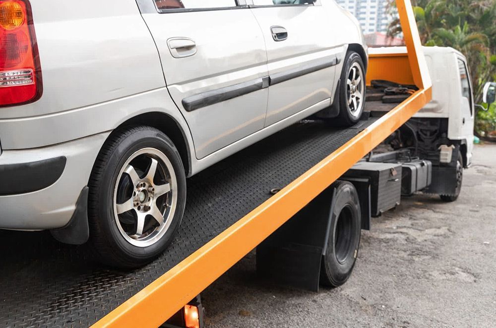A white car is being towed by a tow truck.