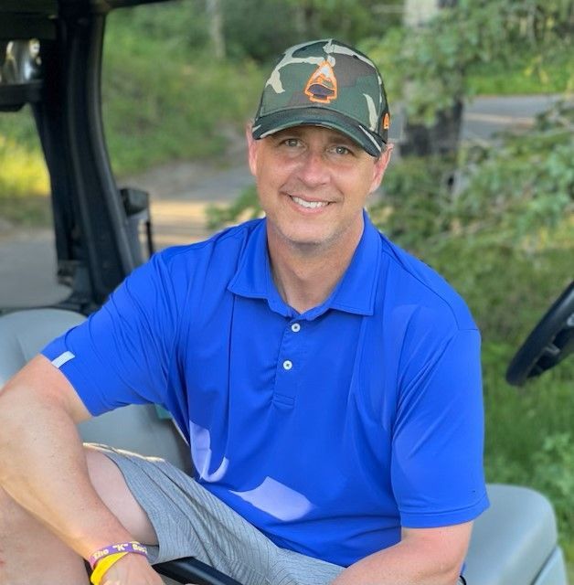 A man in a blue shirt and hat is sitting in a golf cart
