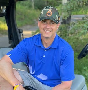 A man in a blue shirt and hat is sitting in a golf cart