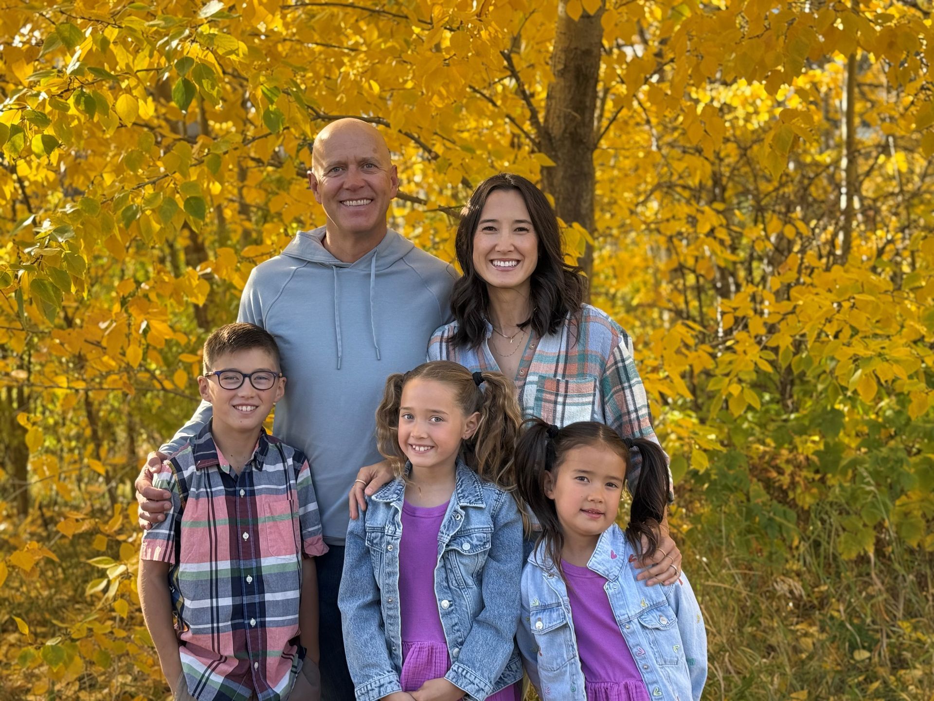 A family is posing for a picture in front of yellow trees.