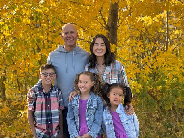 A family is posing for a picture in front of yellow trees.