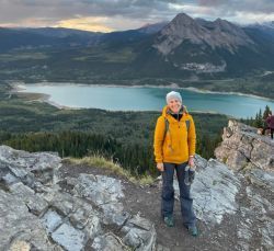 A woman is standing on top of a mountain with a lake in the background.