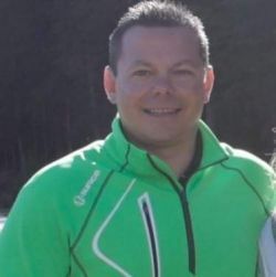 A man in a green jacket is smiling for the camera.