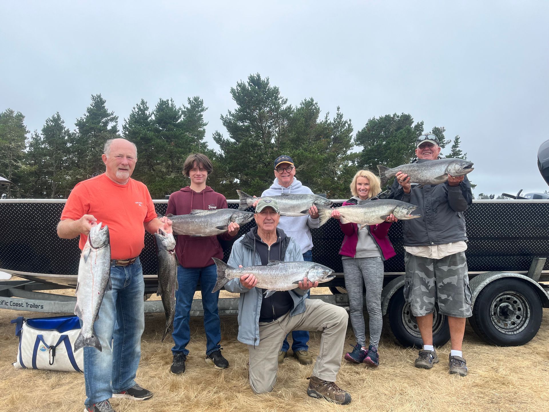 Group of people holding up caught fish near a trailer, possibly at a fishing site.