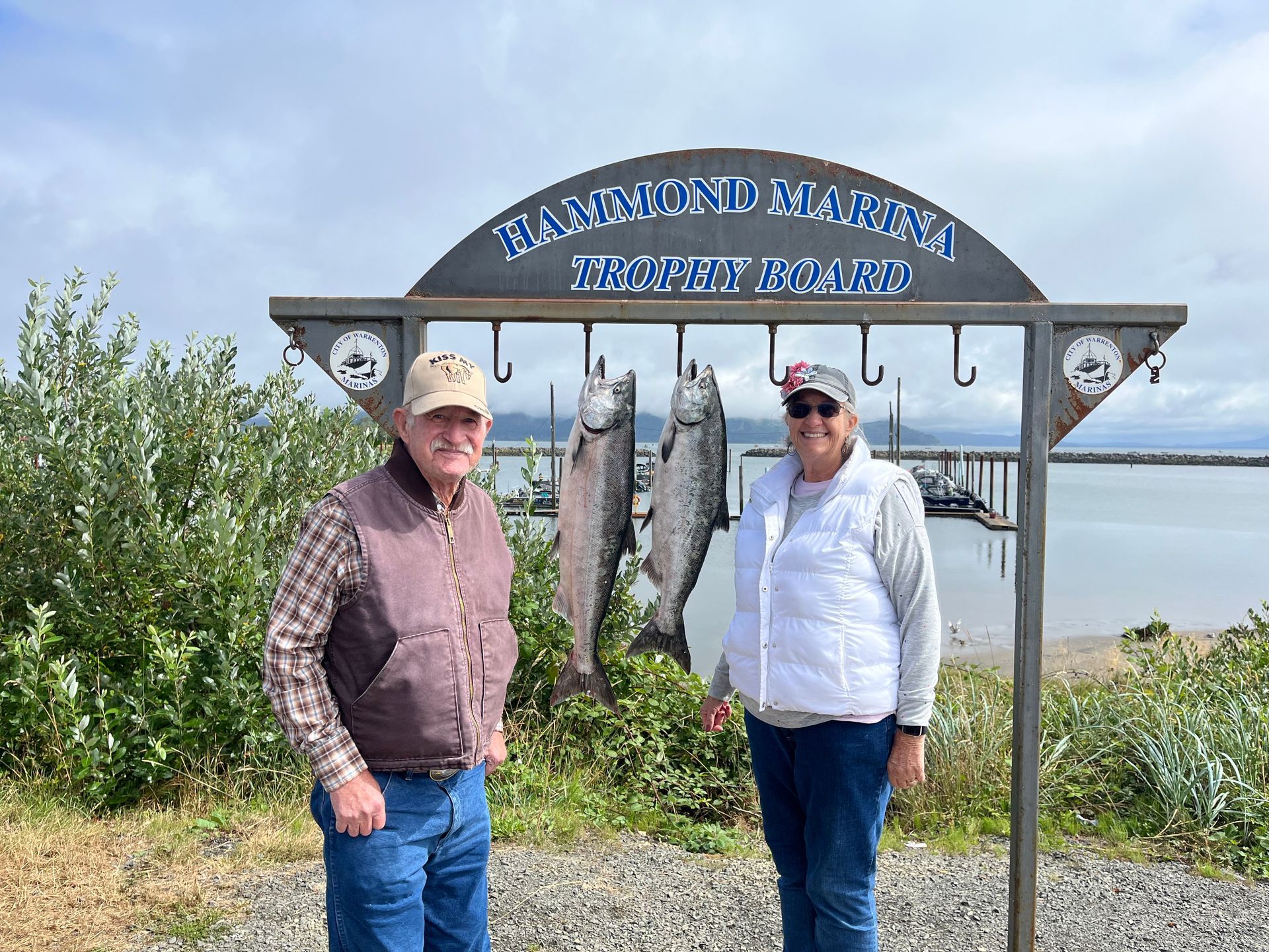 Two people pose with two fish hanging from a sign that reads 