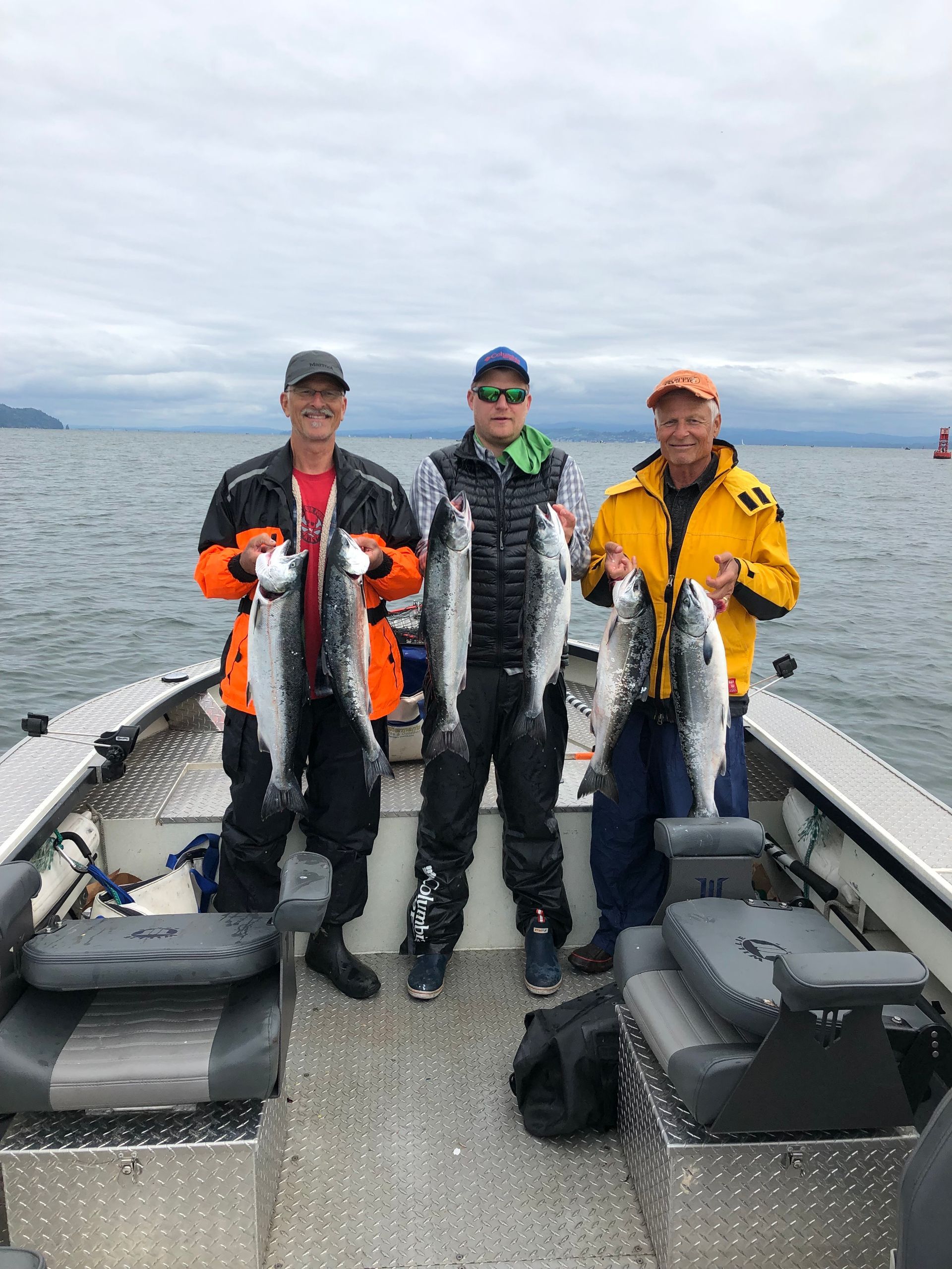 Three people on a boat display their freshly caught fish against an overcast sky.