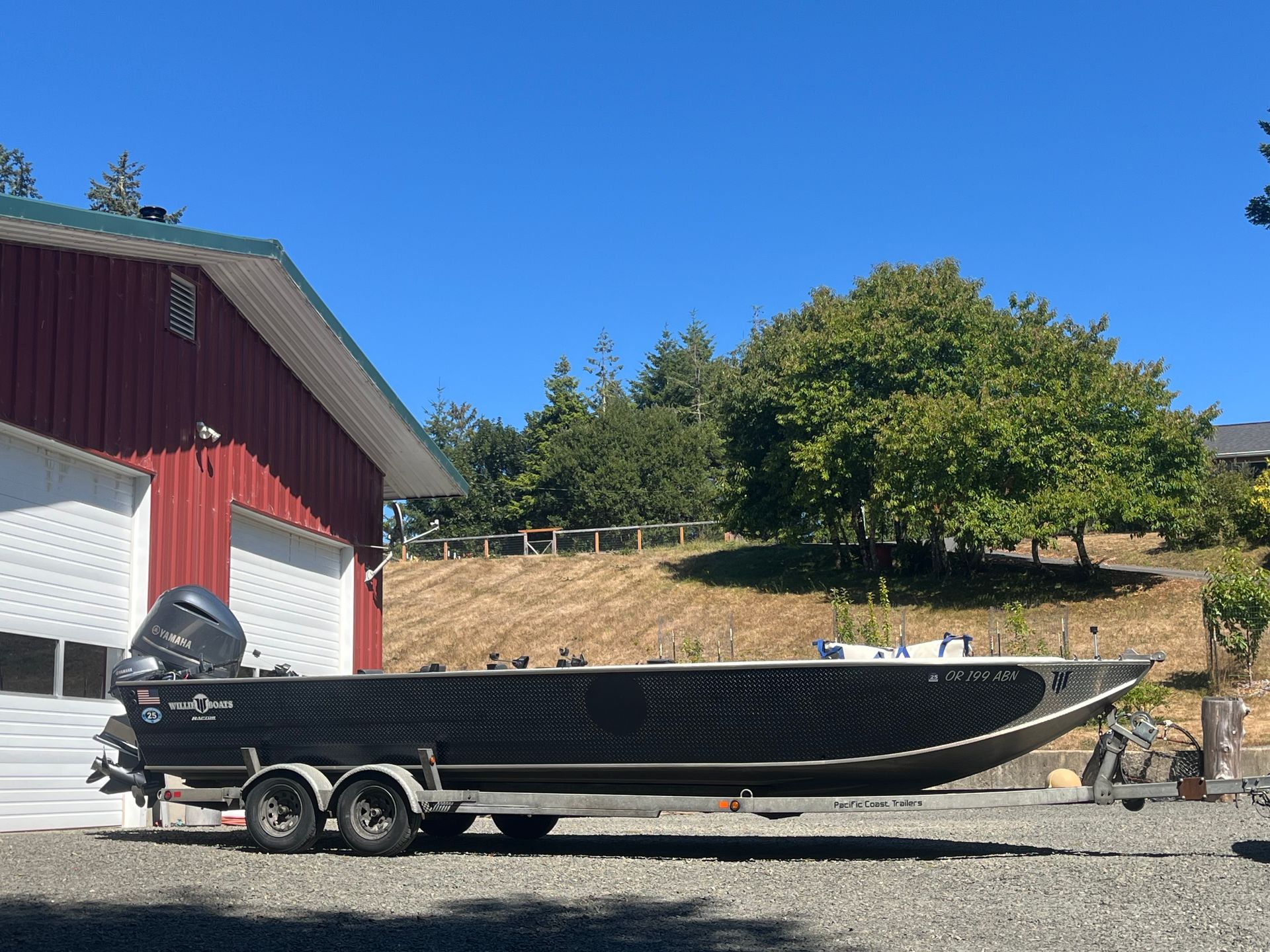 Black fishing boat on trailer in front of a red building and hillside on a sunny day.