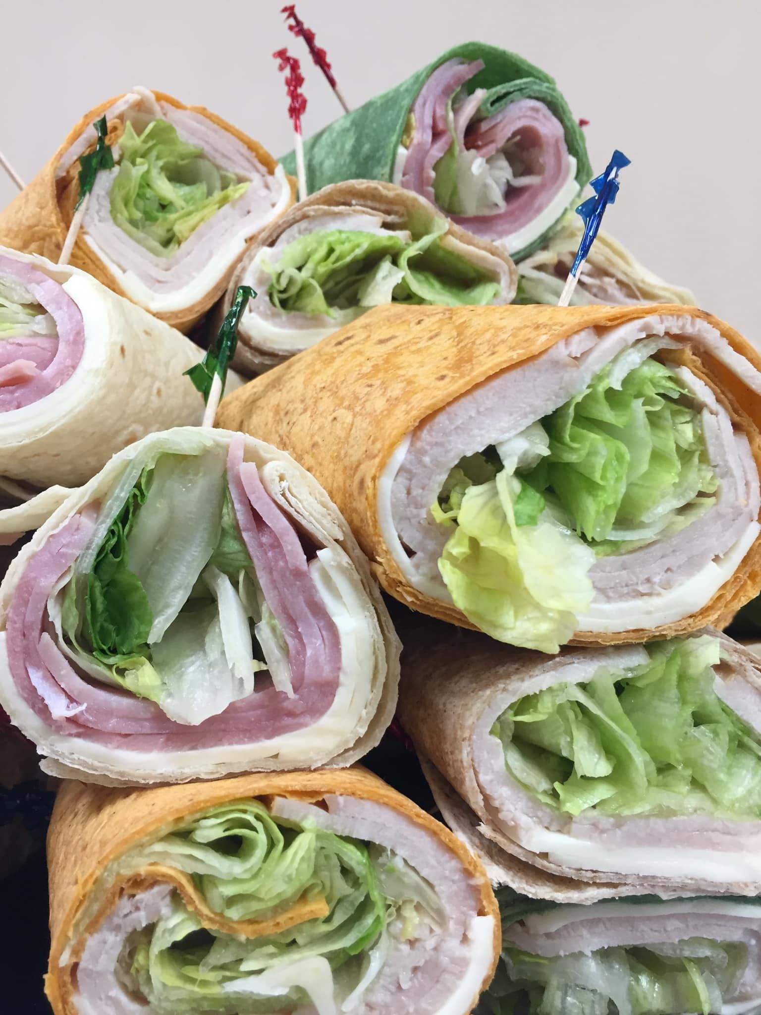 A bunch of wraps with meat and lettuce are stacked on top of each other on a table.