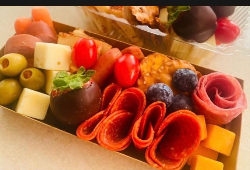 A box filled with a variety of food including strawberries , olives , cheese , and salami.