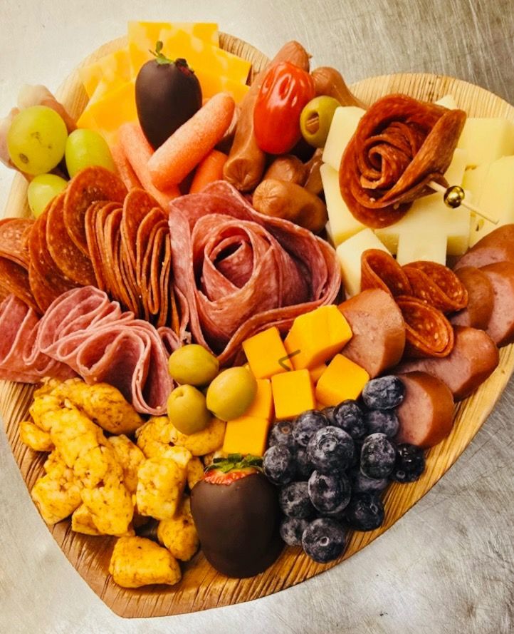 A heart shaped tray filled with meats cheeses and fruit