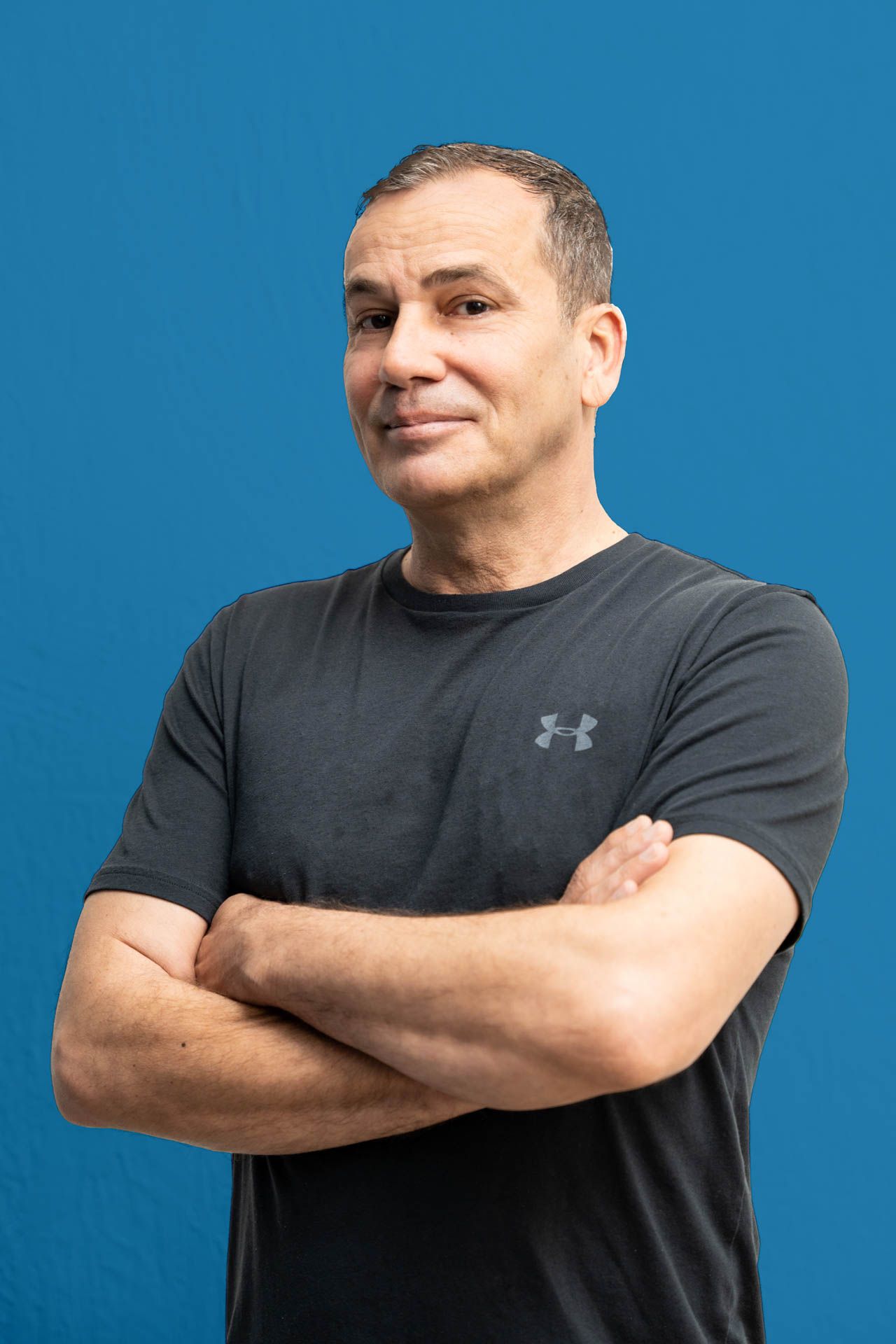 A man in a black under armour shirt is standing with his arms crossed.