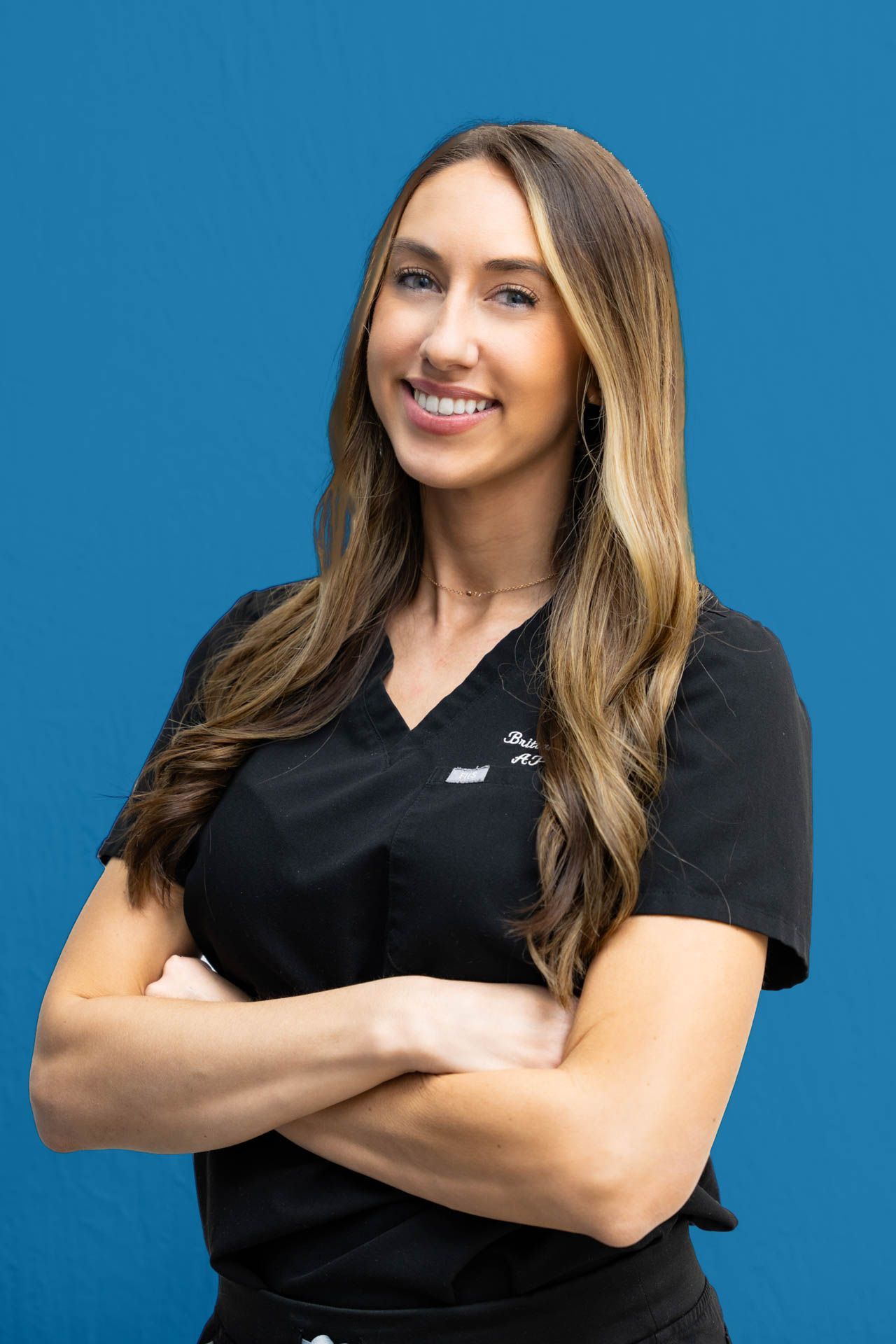 A woman in a black scrub top is posing for a picture with her arms crossed.
