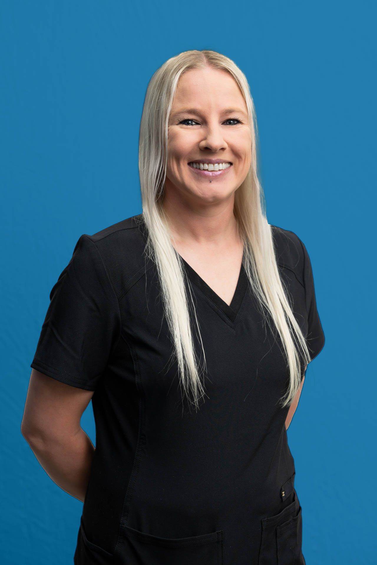A woman in a black scrub top is smiling and standing in front of a blue background.