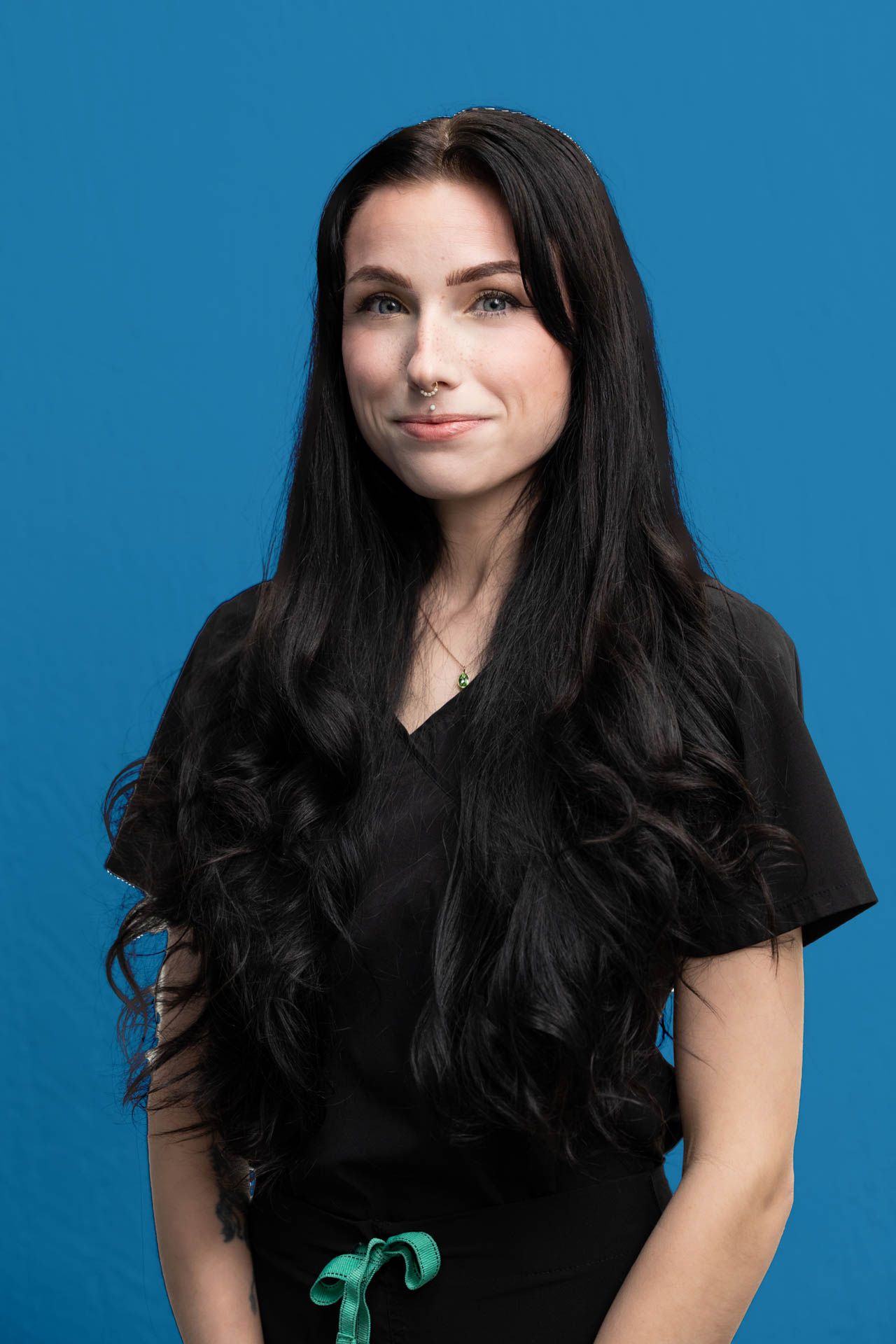 A woman with long black hair is standing in front of a blue background.