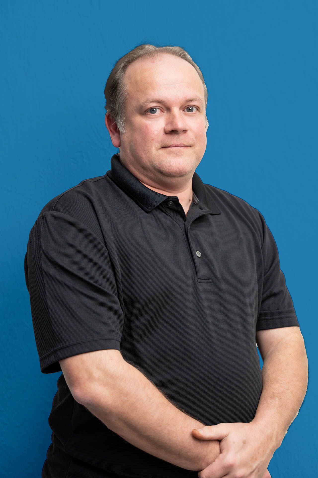A man in a black shirt is standing in front of a blue background.