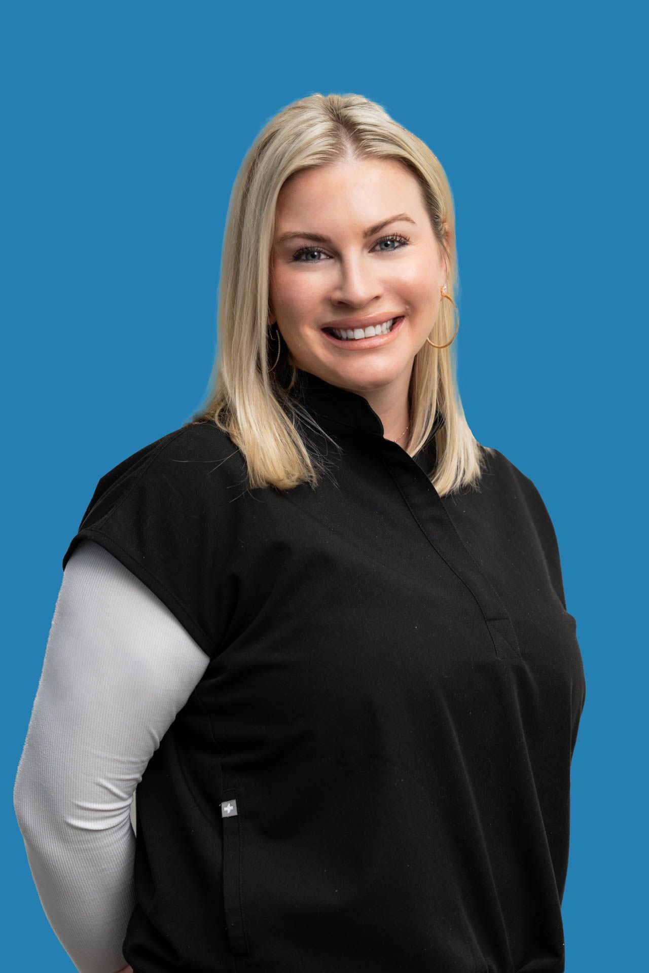 A woman in a black shirt is smiling and standing in front of a blue background.