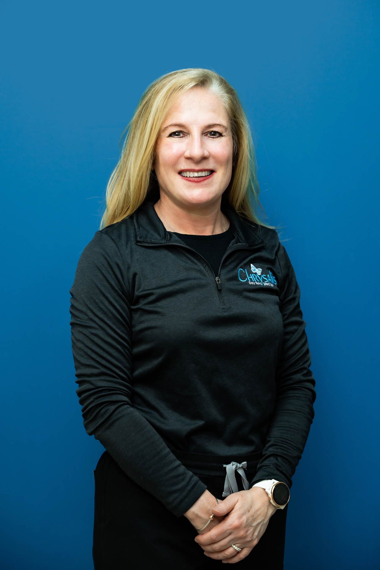 A woman in a black shirt is standing in front of a blue wall.