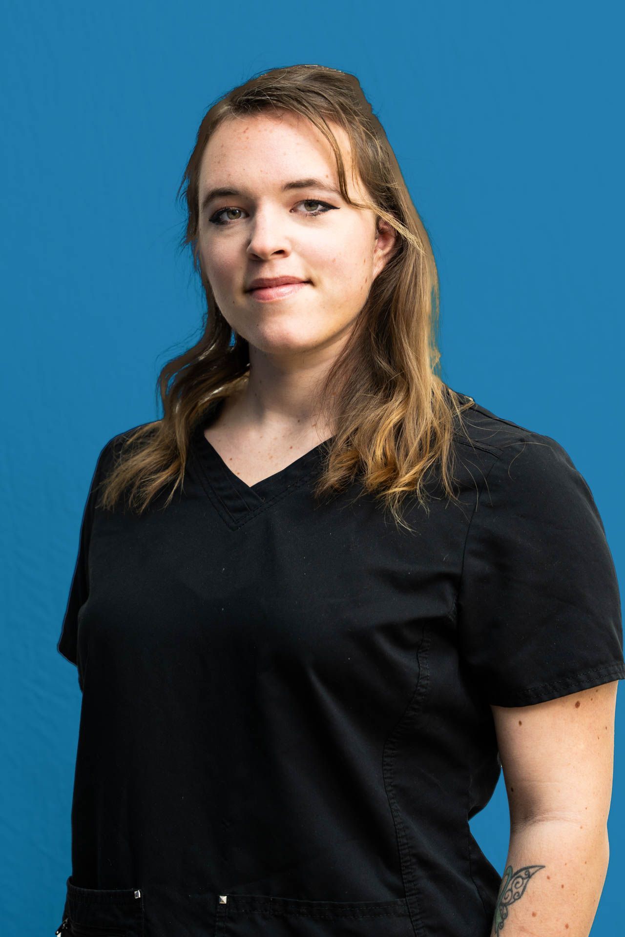 A woman in a black scrub top is standing in front of a blue background.