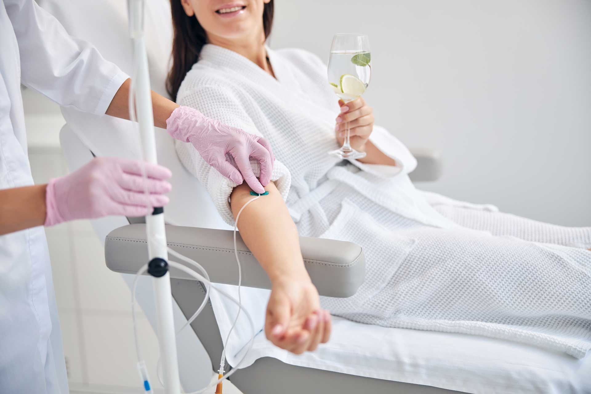 A woman is getting an iv in her arm while holding a glass of champagne.