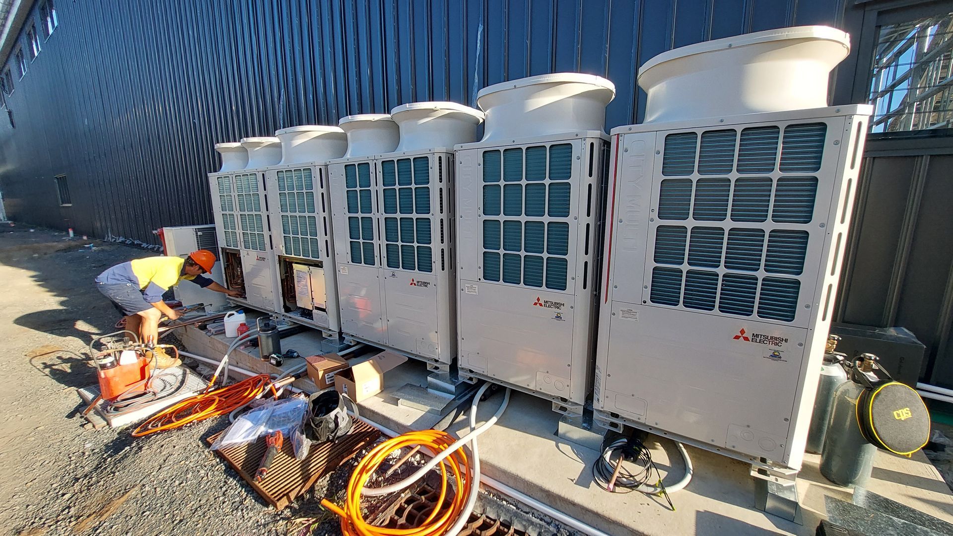 A Man Repairing A Condensor Unit Outside A Large Shed — Frigid-Air PTY Ltd In South Lismore, NSW