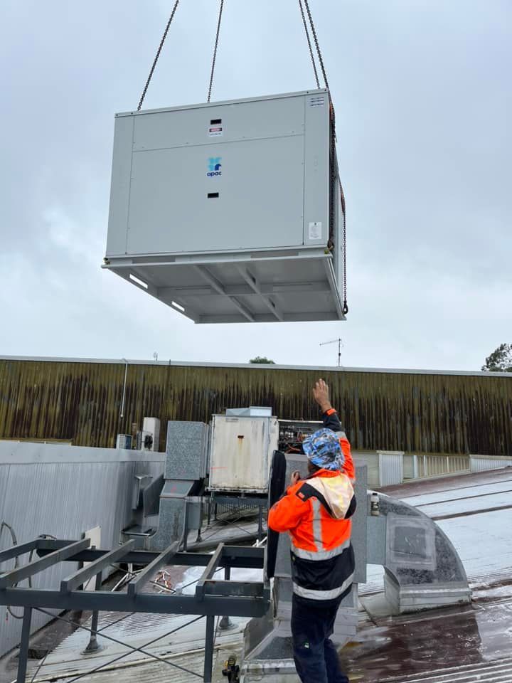 A Man Is Lifting A Large Gray Box From The Roof Of A Building — Frigid-Air PTY Ltd In South Lismore, NSW
