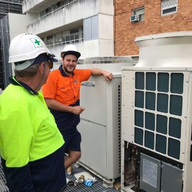 Two Men Wearing Hard Hats Are Standing Next To A Large Air Conditioner — Frigid-Air PTY Ltd In Evans Head, NSW