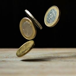 Several coins are falling on a wooden table