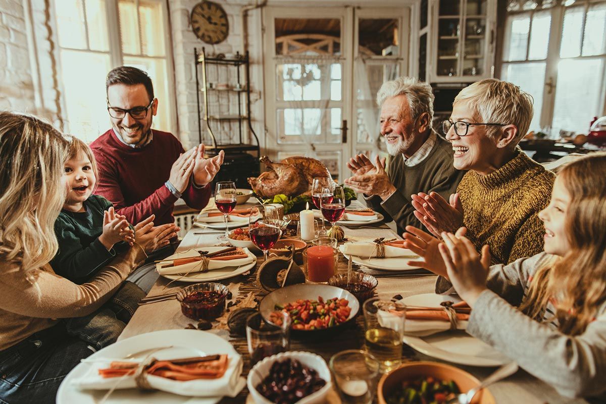 A family is sitting at a table with plates of food and clapping.