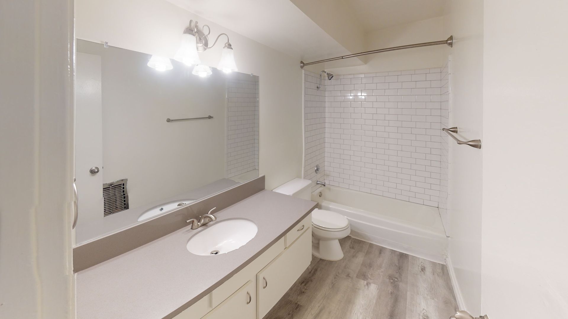 Bathroom with white walls, a long gray countertop with a sink, toilet, and a shower/tub.