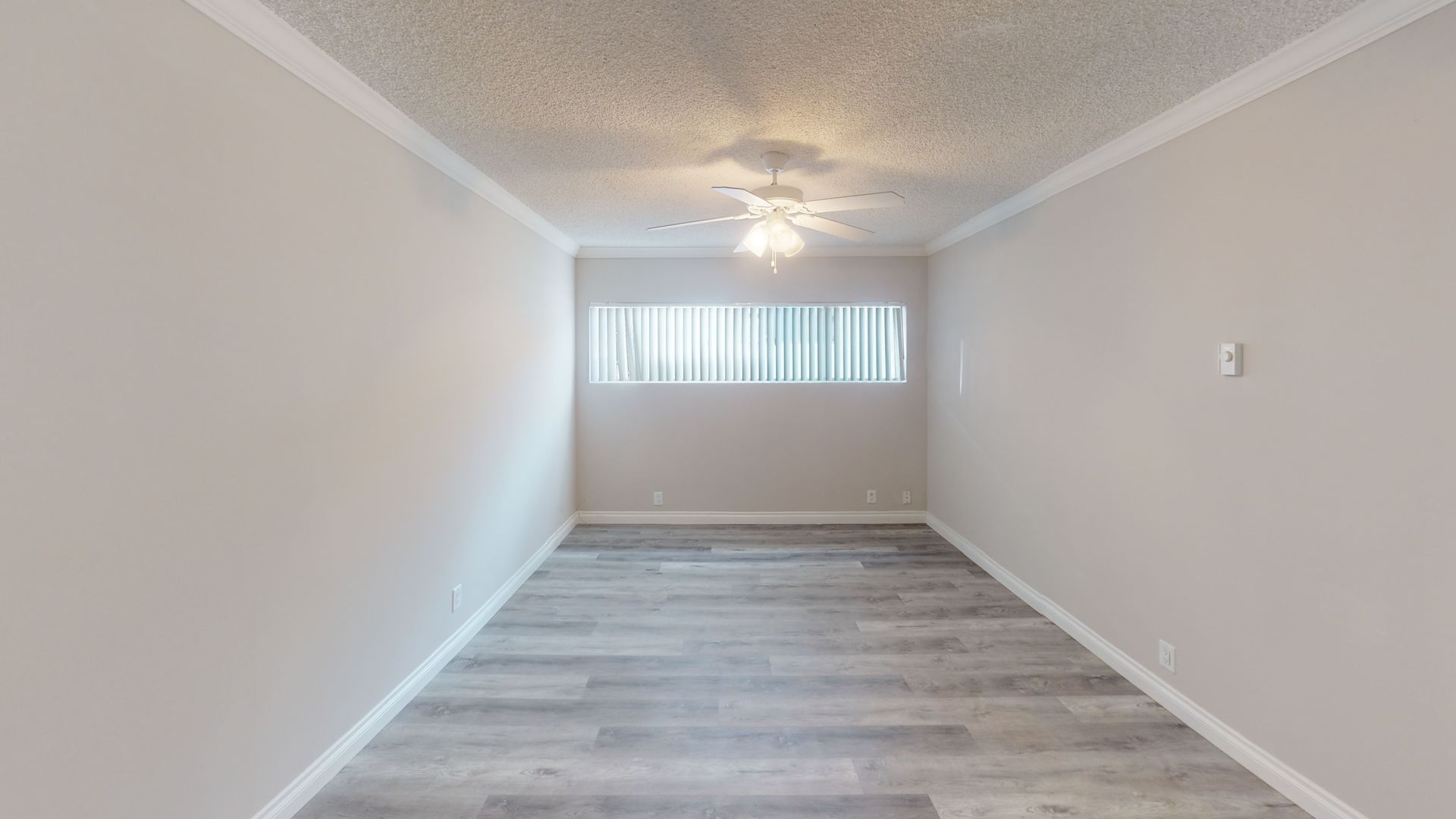 Empty room with gray laminate flooring, white walls, and a window with blinds.