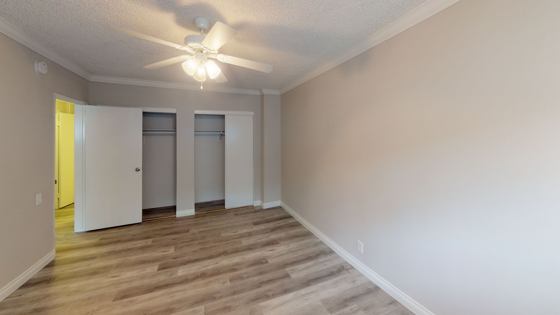 Empty bedroom with wood-look floor, beige walls, two closets, and a ceiling fan.
