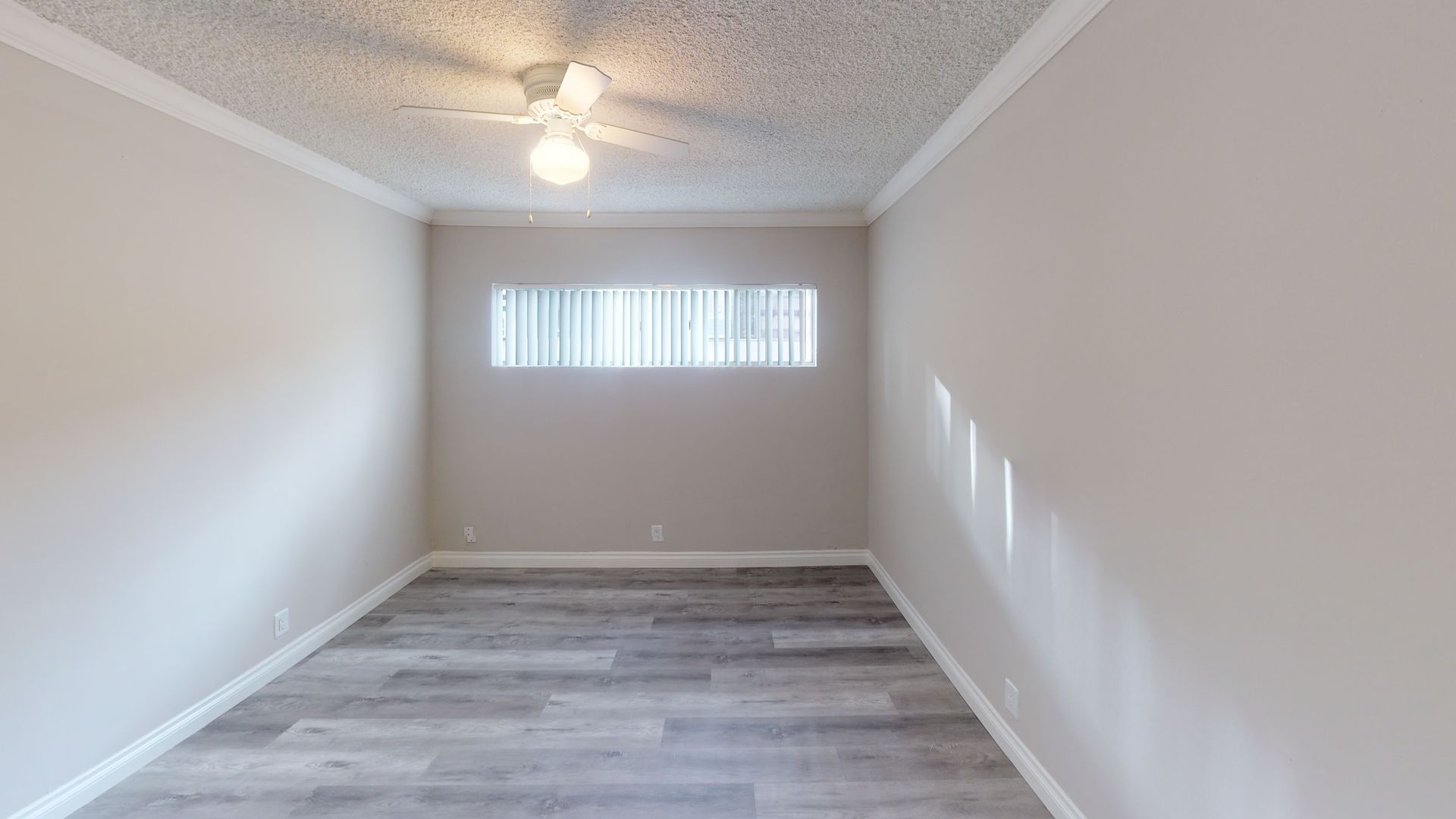Empty room with wood-look floor, window, and ceiling fan. Walls are light beige.