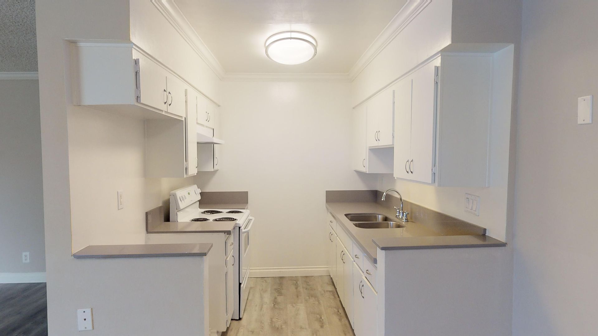 Small, white kitchen with appliances and cabinets; light gray countertops and floors.