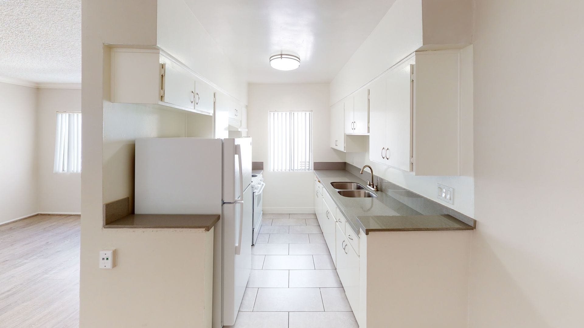 Narrow kitchen with white cabinets, appliances, and countertops. Window in the middle.