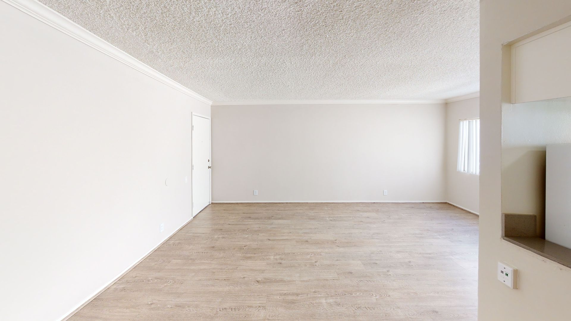 Empty room with white walls, textured ceiling, wooden floor, and a window.