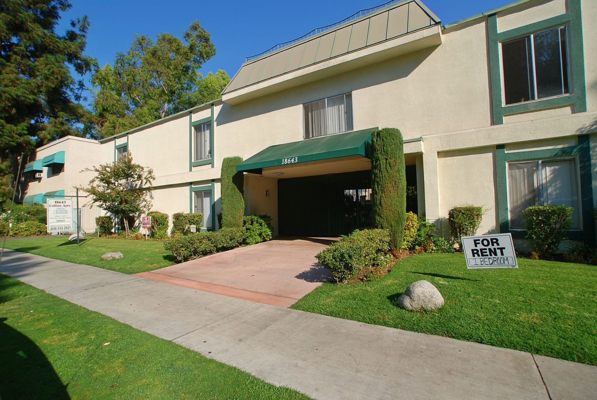 Apartment building with green awnings and trim, a brick driveway, and a 