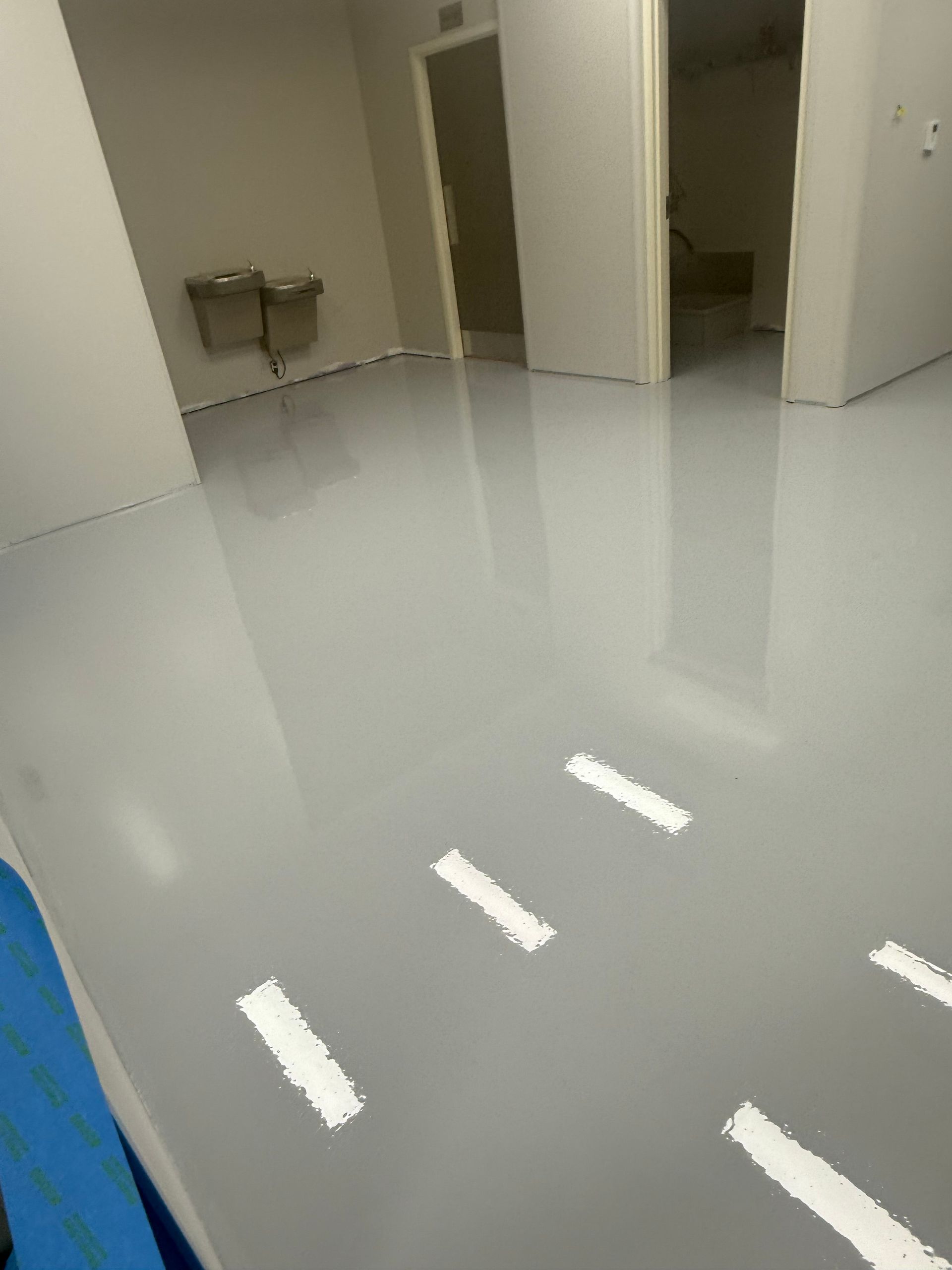 Shiny, light gray epoxy floor in a room with a doorway and a wall-mounted sink.