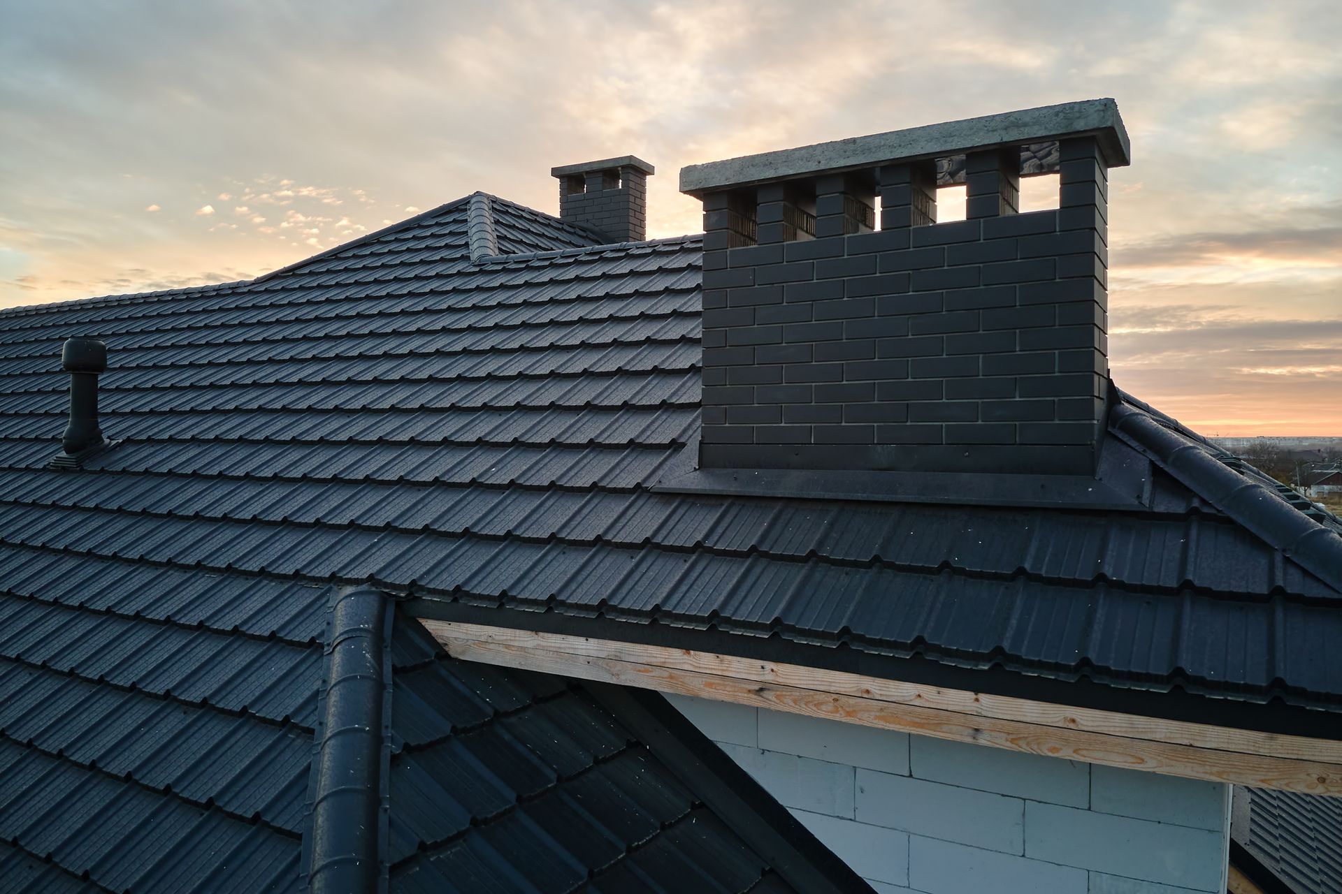 Dark Gray Metal Roof With Two Chimneys Against an Evening Sky — Callaway Roofing & Construction in Bathurst, NSW