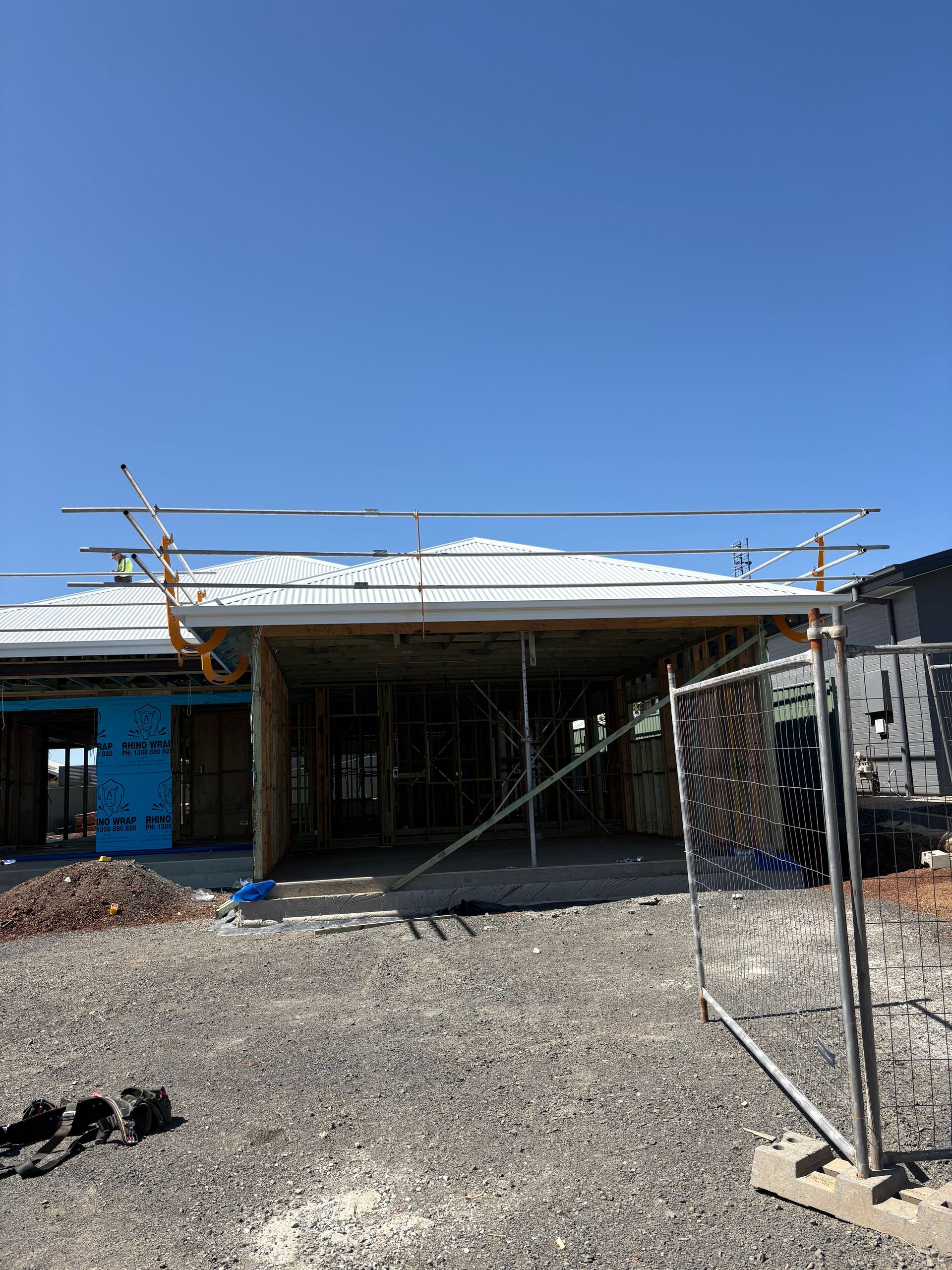 A house under construction with scaffolding, gravel ground, and a blue sky.