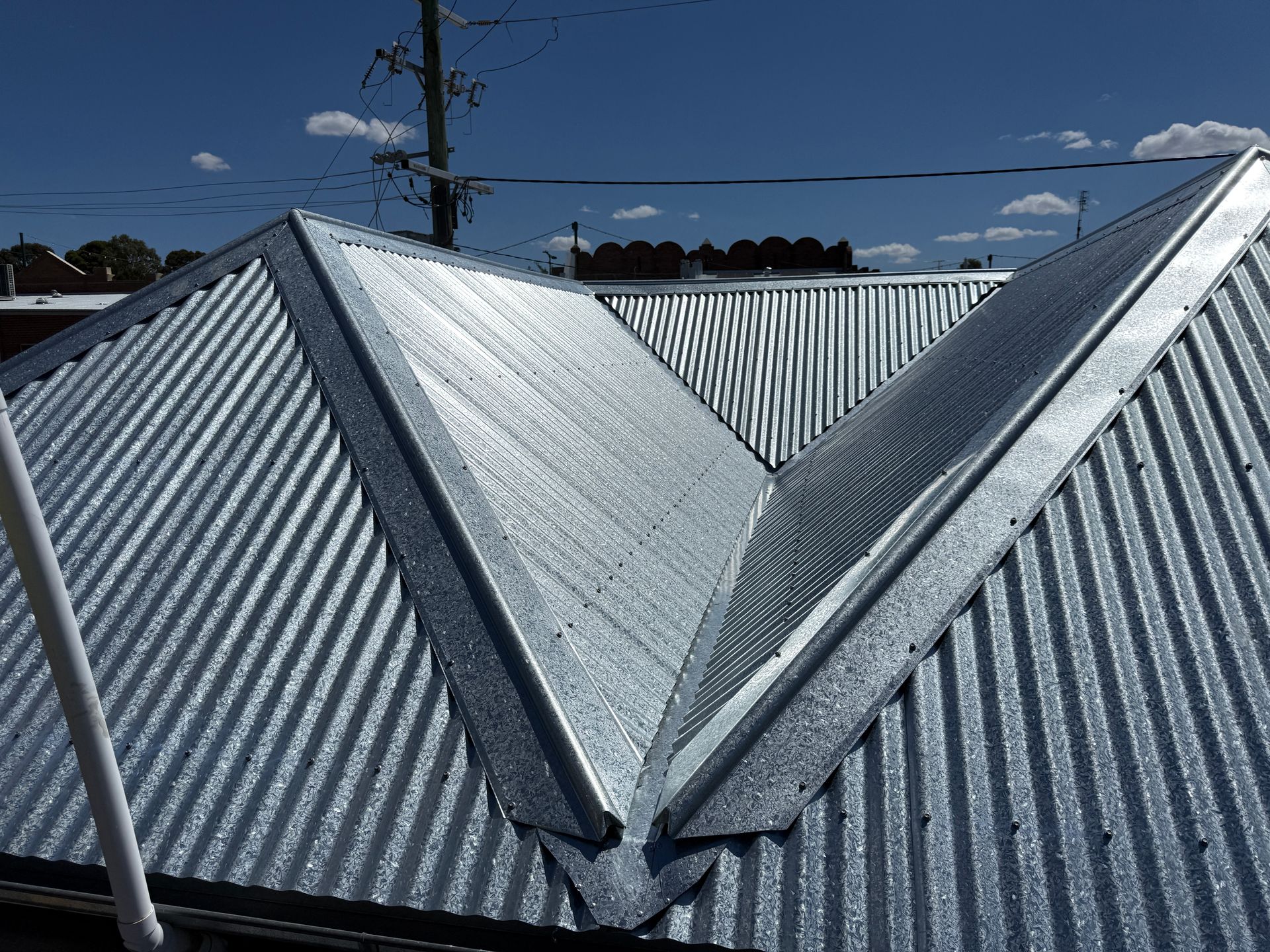 Corrugated metal roof, silver, with a valley and angled ridges. Blue sky in the background.