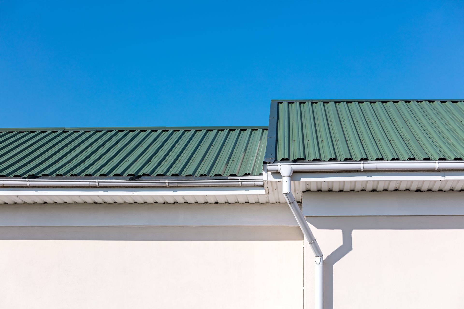Green Corrugated Metal Roof With White Trim and Gutter Against a Blue Sky — Callaway Roofing & Construction in Parkes, NSW