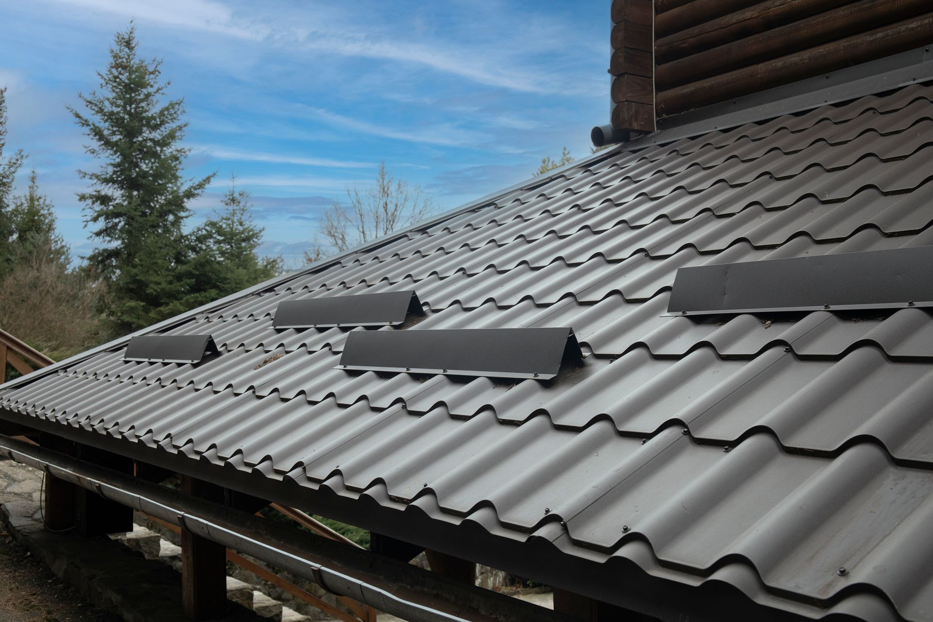 Metal Roof With Vent Stacks, Against a Blue Sky, Near a Log Building — Callaway Roofing & Construction in Coonamble, NSW