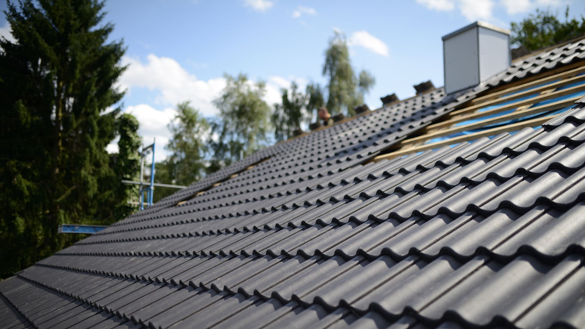 Dark Gray Roof Tiles Being Installed, With Visible Underlayment And Chimney Against A Blue Sky — Callaway Roofing & Construction in Gunnedah, NSW