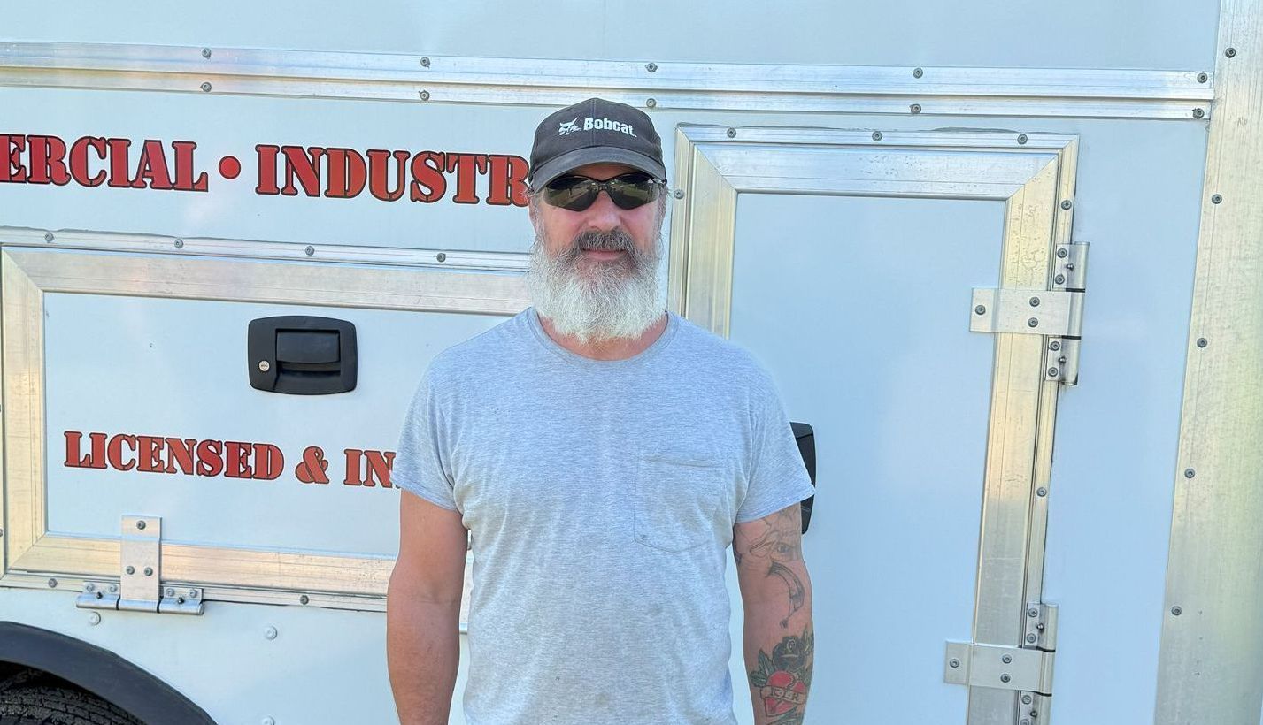 A man with a beard is standing in front of a trailer.