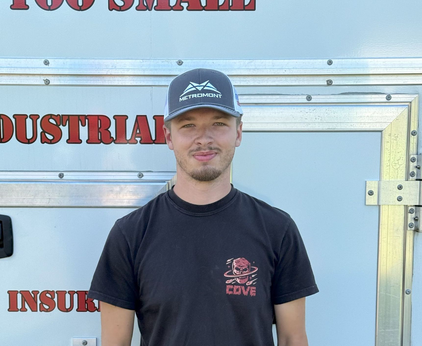 A man wearing a hat and a black shirt is standing in front of a trailer.