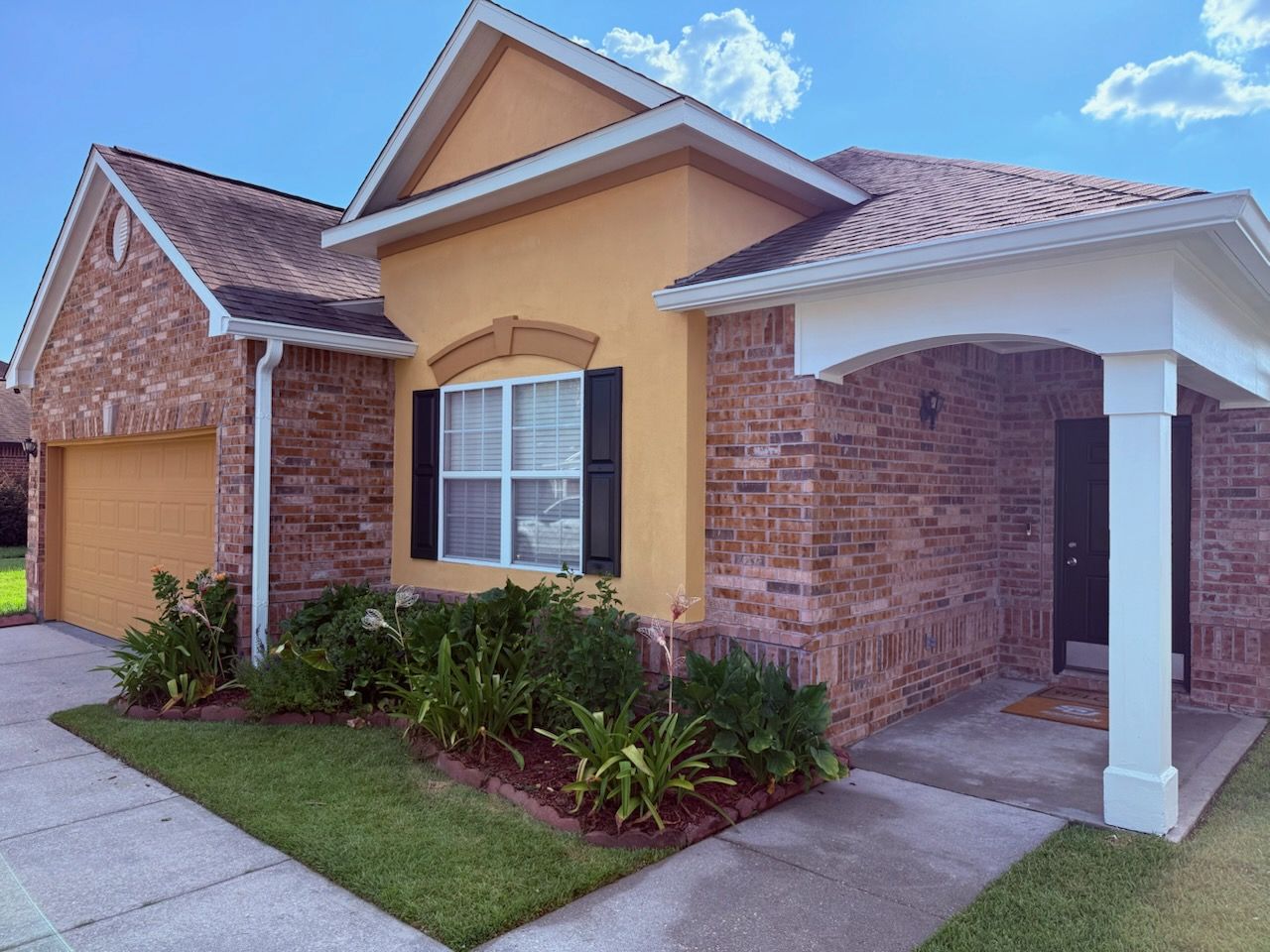 Exterior of a brick and stucco house with a garage and green landscaping under a blue sky.