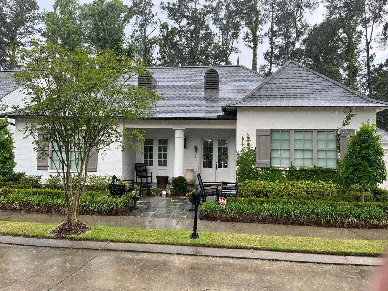 White house with gray roof, green shrubbery, and mailbox in front.