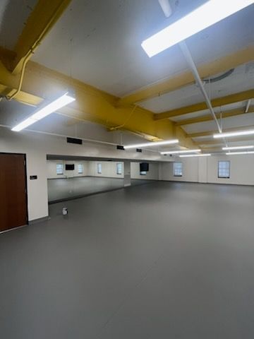 Empty studio with mirrored wall, dark floor, and yellow beams.